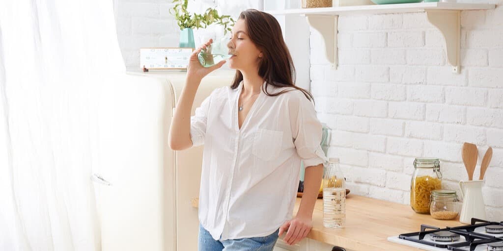 Kobieta stojąca w kuchni i pijąca wodę, ponieważ czuje słodki posmak w ustach.